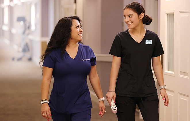 Two uniformed staff members walking down a hallway and smiling at each other